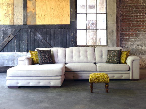 Aymee corner sofa with padded details in a light beige fabric with gray and yellow decorative cushions