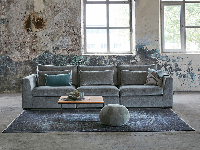 Breites Sofa mit bequemen Sitzen. Blau/grauer Stoff und ein großer Teppich.
