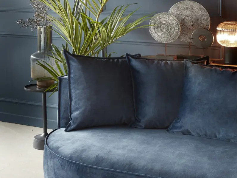 Velvet donker blauwe tweezitsbank met ronde vormen en bijhorende rugkussens. Gestyled met een rond vloerkleed en planten.