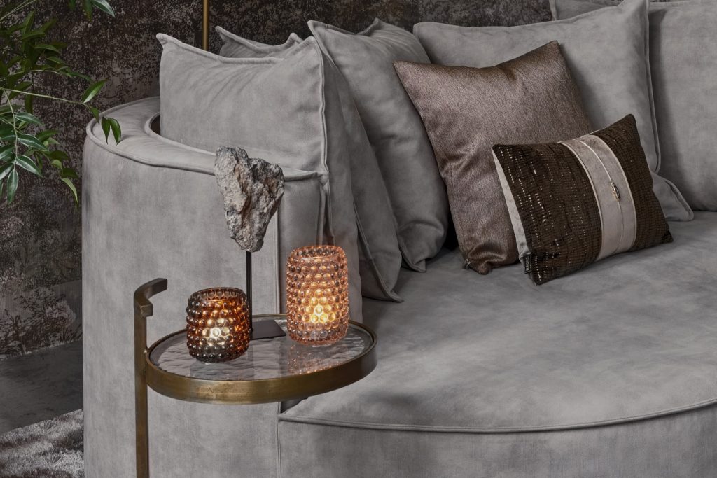 Lounge-Sofa mit organischen Formen und passenden Rückenkissen aus grauem Samtstoff sowie Gold- und Bronzeaccessoires.