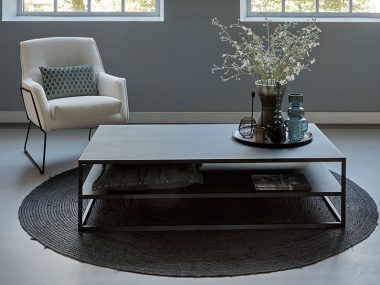 Tavolino da caffè nero in metallo pesante 140 cm, con poltrona bouclè e tappeto rotondo.