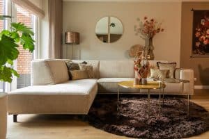 Inside view with corner sofa Sophie in a beige fabric and with a round rug.