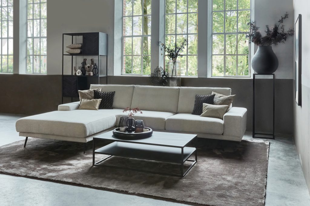 Canapé d'angle Rosalie en tissu beige. Décoré avec des meubles en métal noir et un grand tapis.