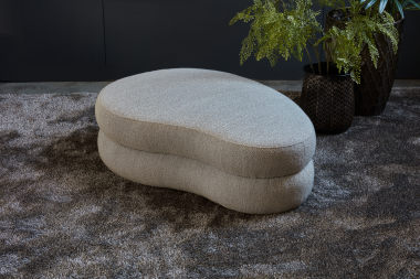 Hocker Bubble Curve, a footstool with organic shapes in a beige fabric.