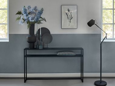 Heavy metal side table with black vase with blue artificial flowers.