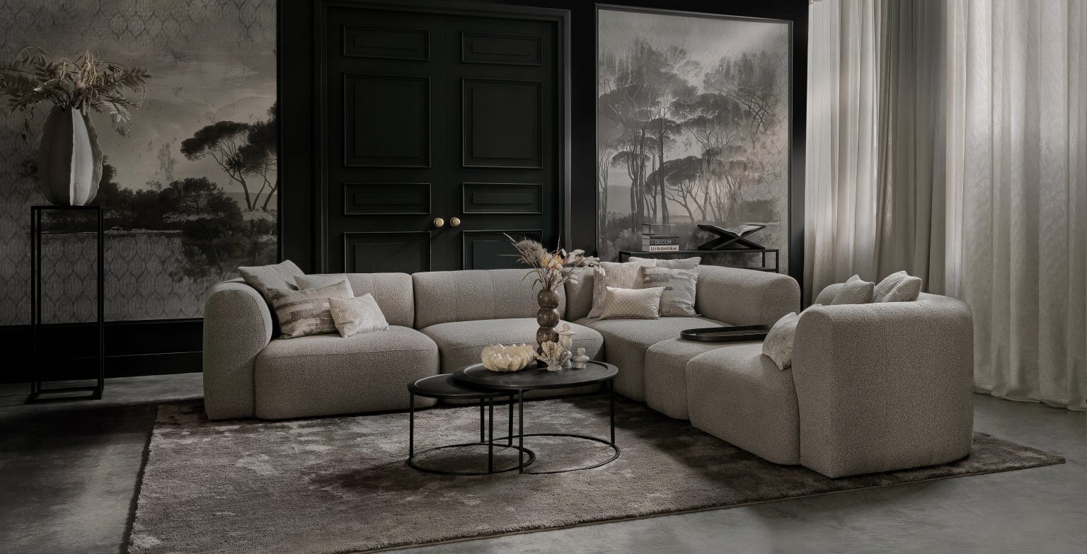 Beige elementenbank met ronde vormen in de armleuning en rugleuning. Gestyled met natuurlijke materialen en beige en zwarte woonaccessoires.