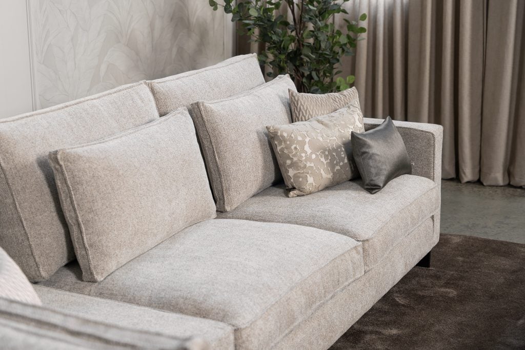 Ecksofa Gigi in einem neutralen Beigeton, mit Accessoires in warmen Erdtönen gestylt.