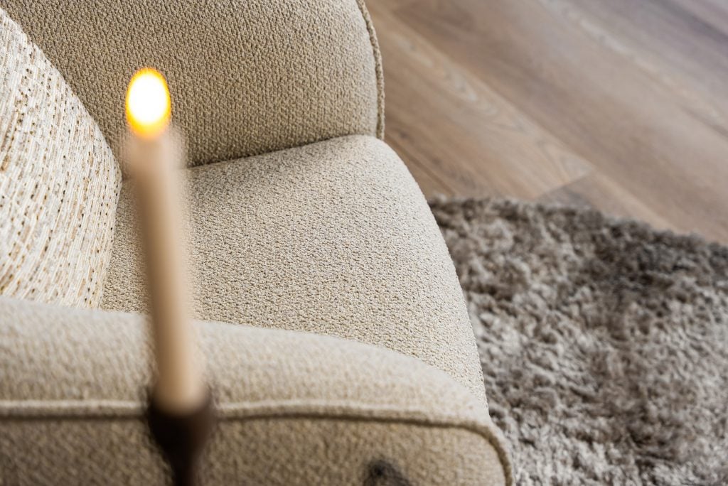 Lio draaifauteuil van Gusj in lichte bouclé stof met anodic brown draaionderstel op een rond vloerkleed in een warm interieur.