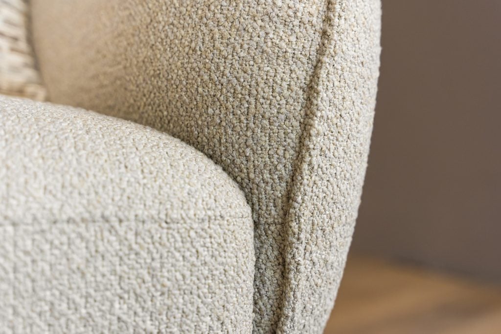 Lio draaifauteuil van Gusj in lichte bouclé stof met anodic brown draaionderstel op een rond vloerkleed in een warm interieur.
